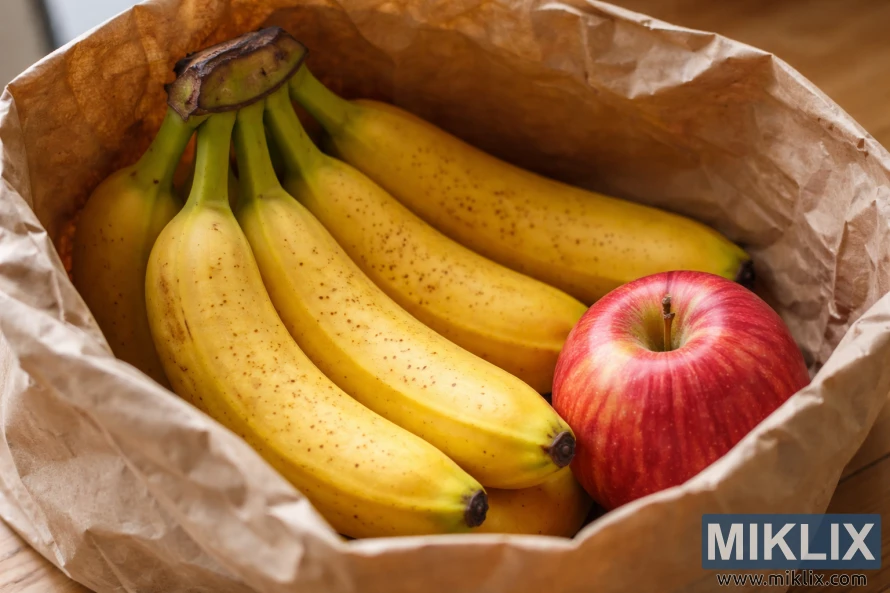 Ripe yellow bananas and a red apple resting together inside an open brown paper bag under warm light